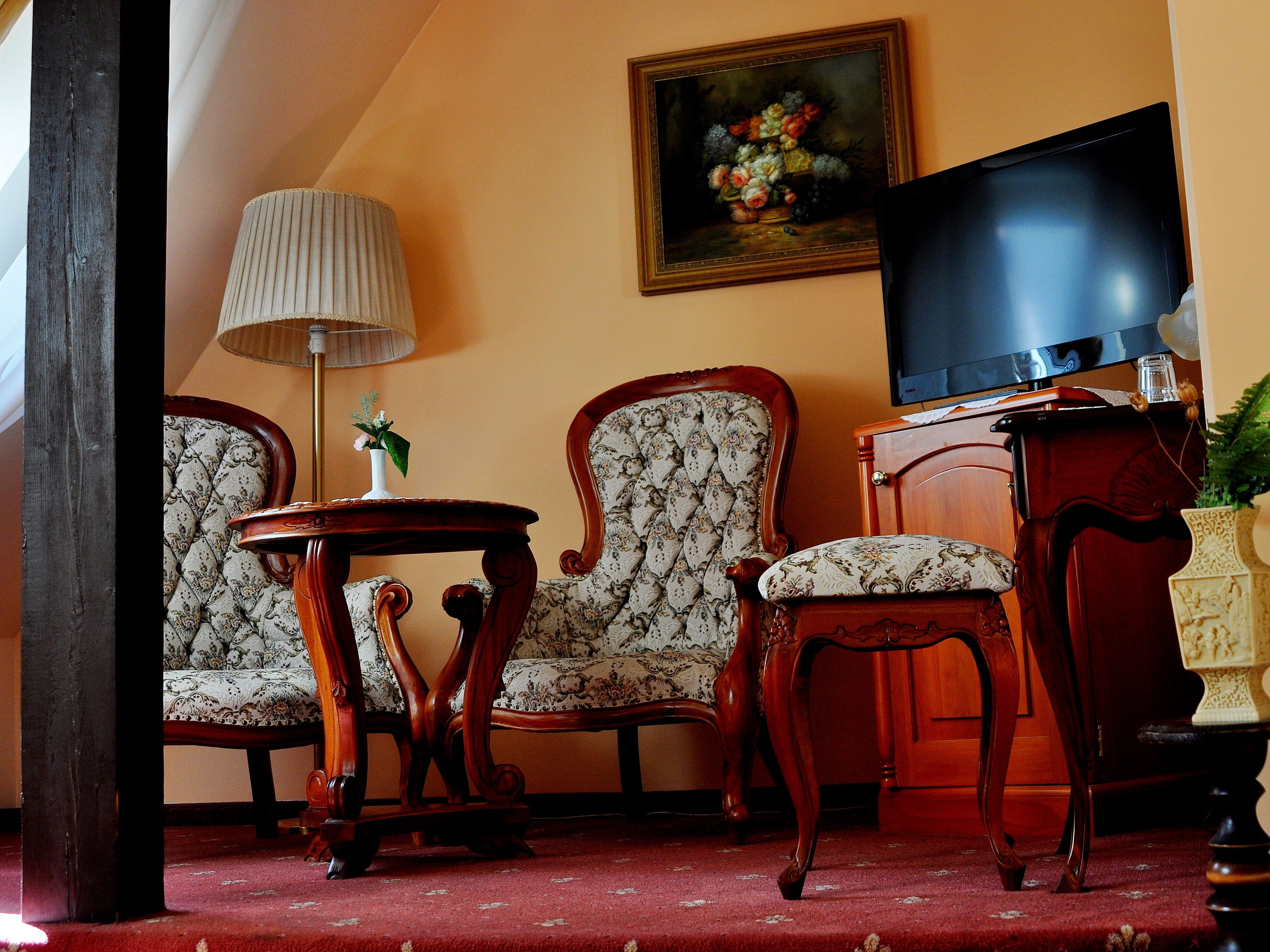 Une pièce comprenant deux fauteuils rembourrés, une table d’appoint en bois, un lampadaire, un téléviseur et un tableau accroché au mur.