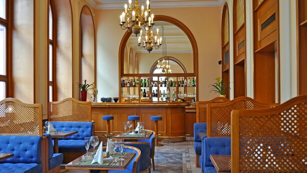 Zona de bar con asientos tapizados en azul, barra con botellas y candelabro.