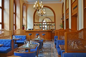Zona de bar con asientos tapizados en azul, barra con botellas y candelabro.