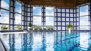 Una piscina interior con agua azul cristalina, ventanas amplias y sillas de descanso.