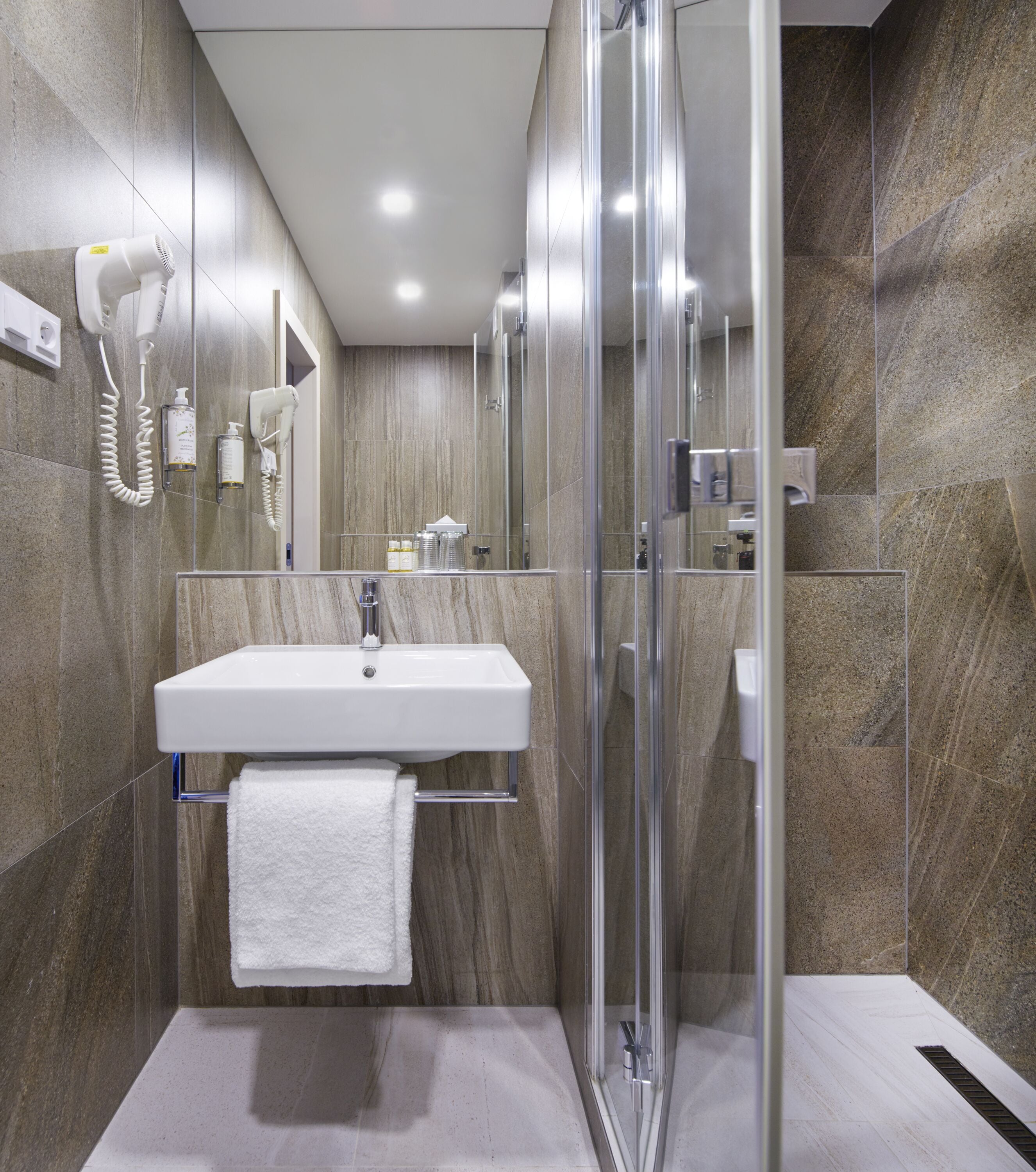 A modern bathroom with a glass shower enclosure, a white sink, and a towel hanging on a rack.