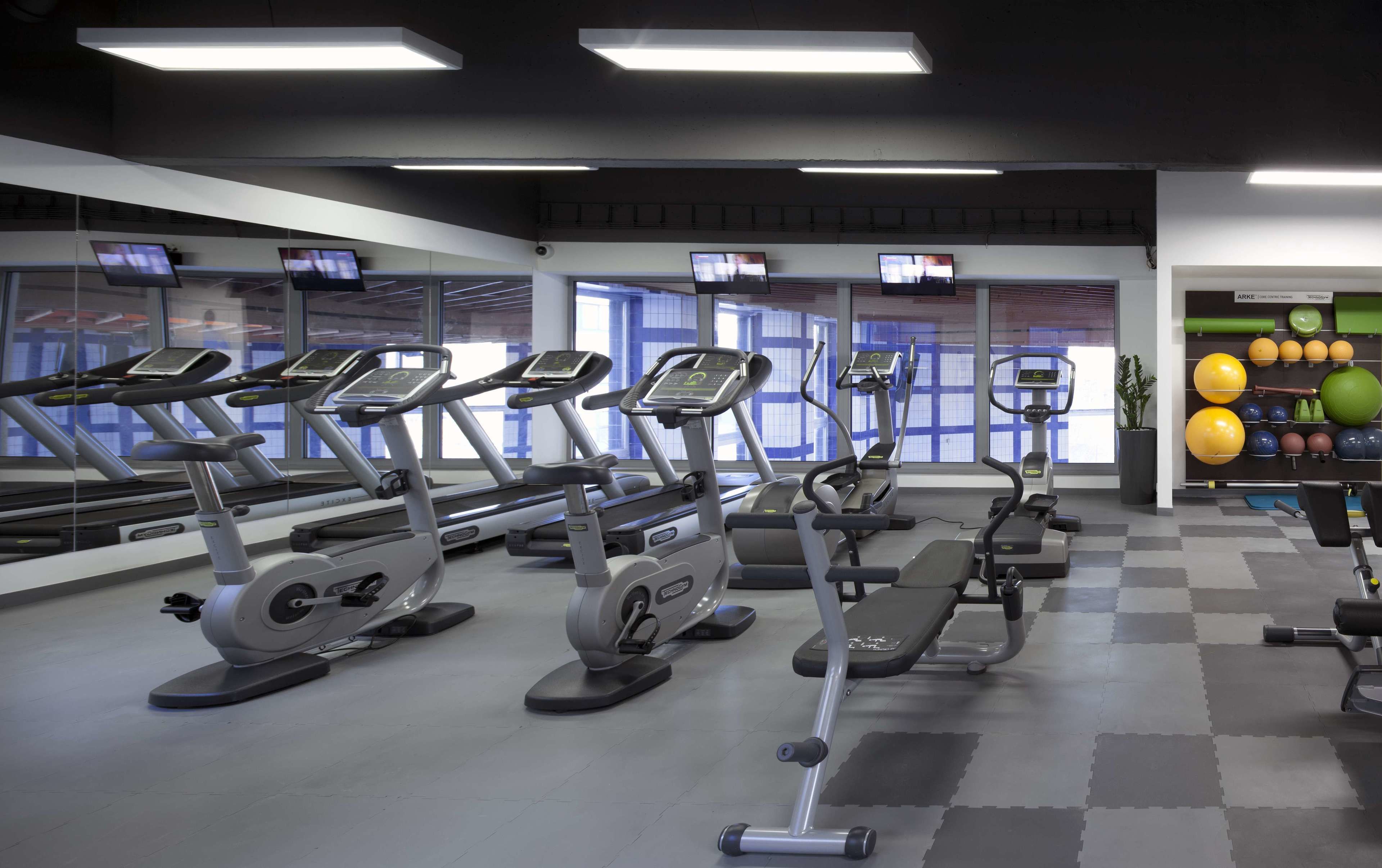 Un gimnasio con cintas de correr, bicicletas estáticas y una pared llena de pelotas de ejercicio.
