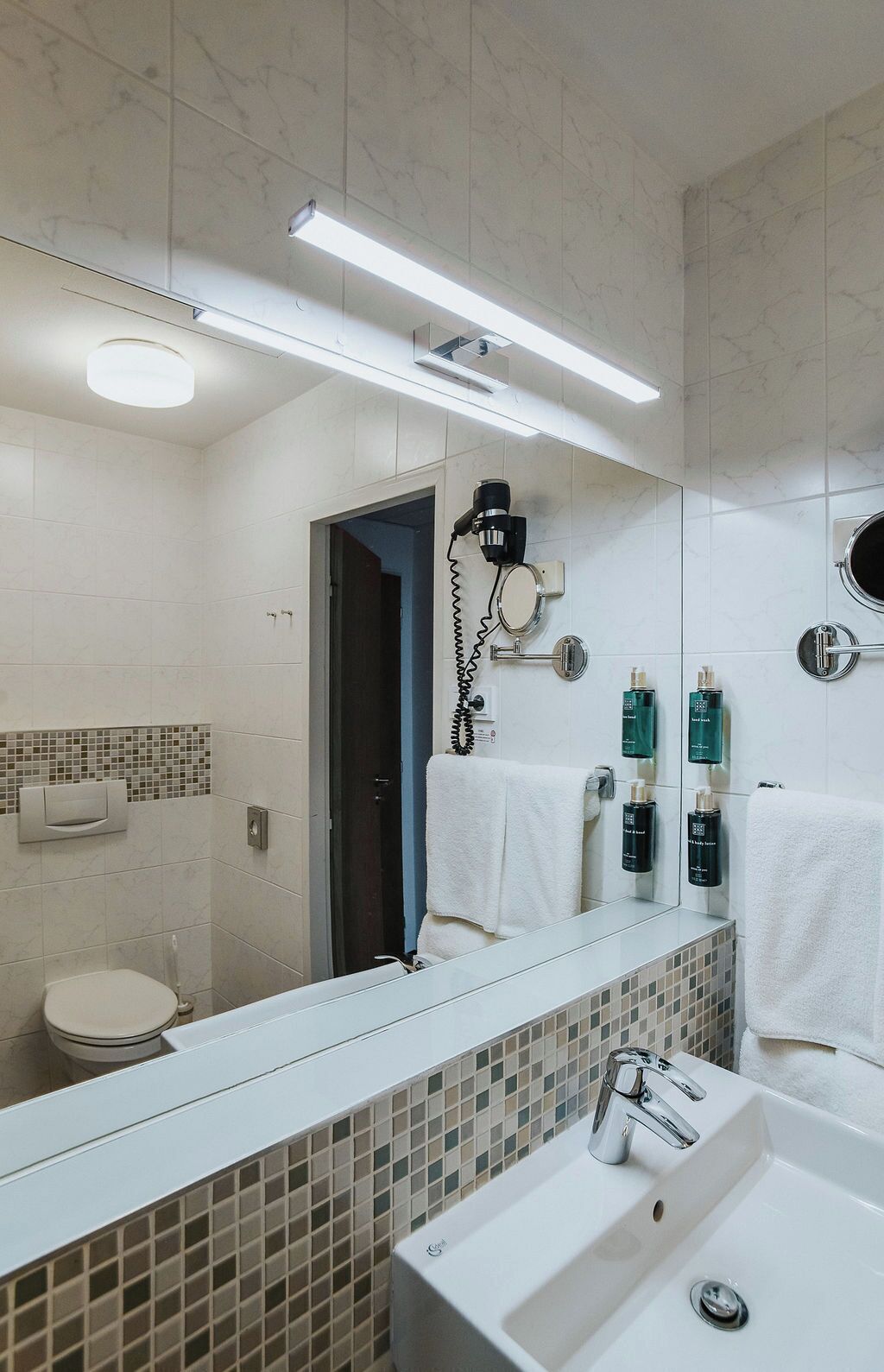 A modern bathroom with a large mirror, a sink, and a hairdryer mounted on the wall.