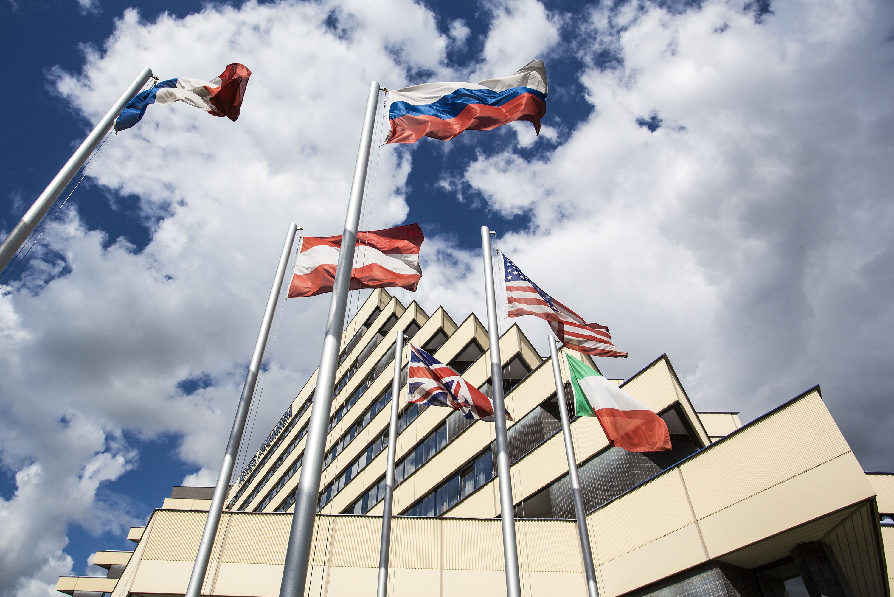 Un edificio con varias banderas en mástiles, incluyendo la bandera estadounidense, la Union Jack y la bandera italiana.