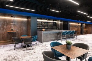 Een moderne bar met een toog, zitplaatsen en diverse flessen op planken.