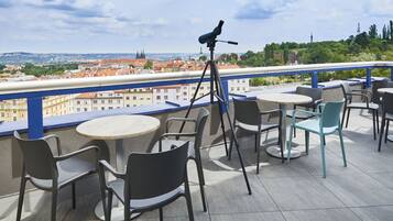 Una terraza con asientos al aire libre, un telescopio y vistas de un paisaje urbano con edificios históricos.