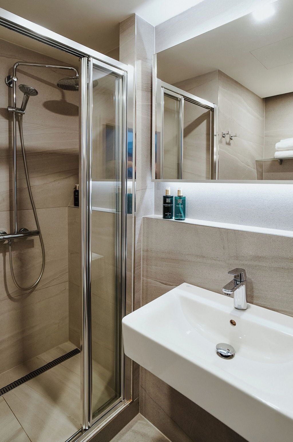 A modern bathroom with a glass-enclosed shower, a white sink, and a mirror above the sink.