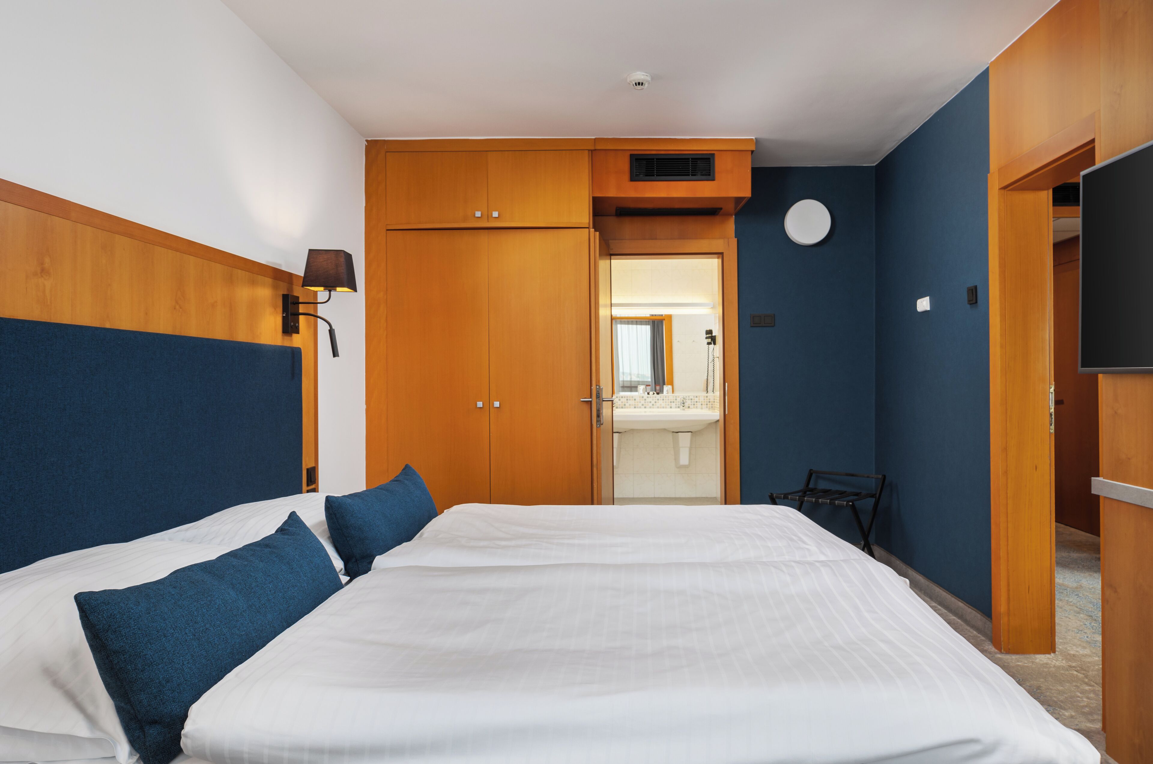 Habitación de hotel con una cama grande, armario de madera, baño pequeño y televisor.