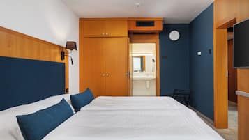 Habitación de hotel con una cama grande, armario de madera, baño pequeño y televisor.