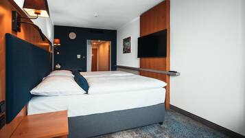 Una habitación de hotel moderna con una cama grande, mesitas de noche, un televisor de pantalla plana montado en la pared y un cabecero de madera.