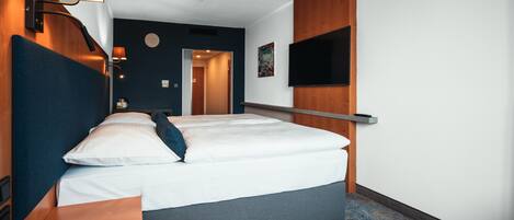 Una habitación de hotel moderna con una cama grande, mesitas de noche, un televisor de pantalla plana montado en la pared y un cabecero de madera.