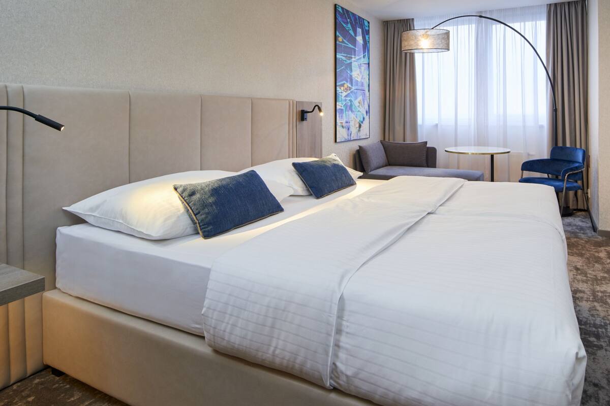 A hotel room with a large bed, a desk, a chair, and a painting on the wall.