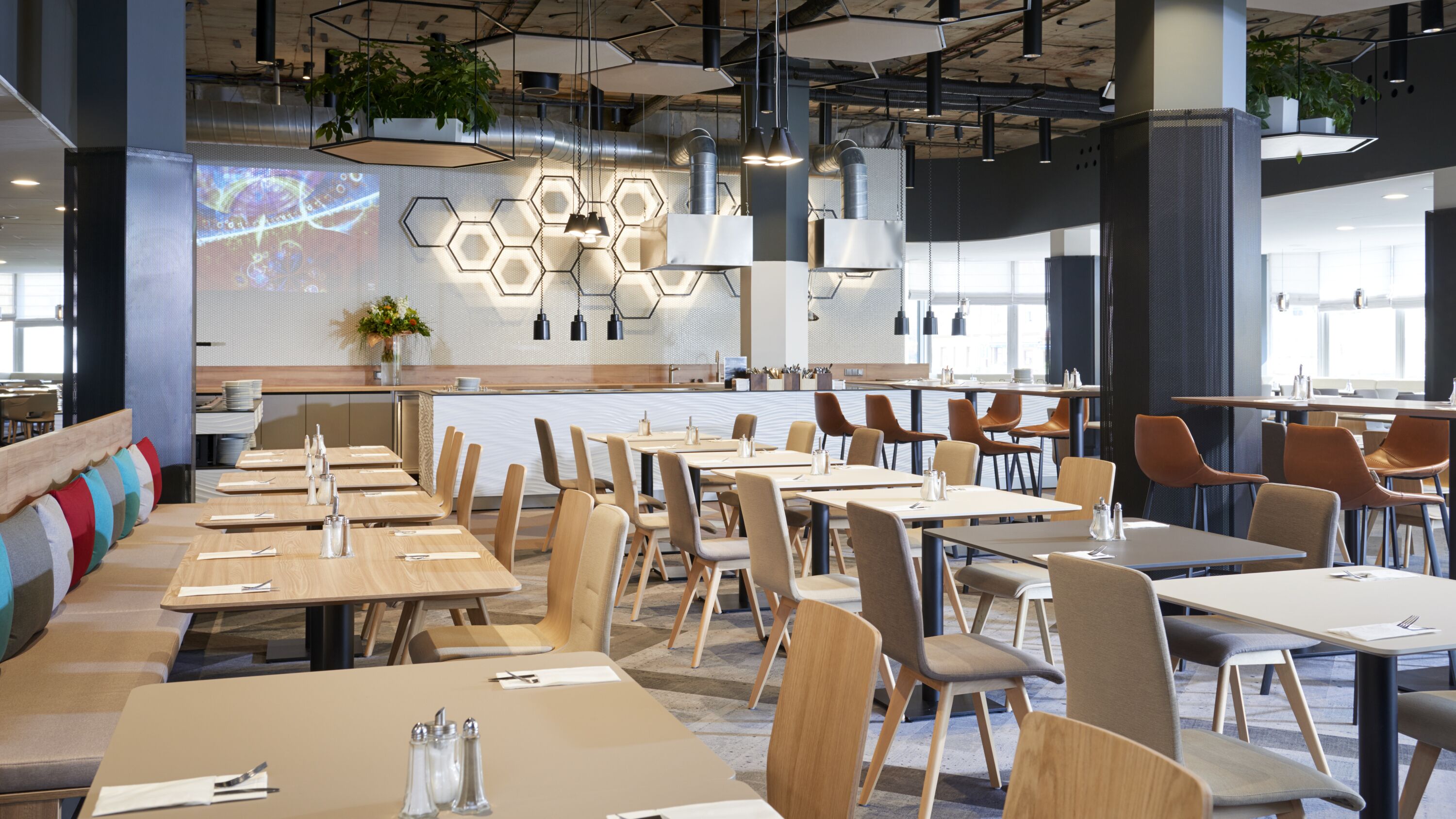 Ein modernes Restaurant mit langen Gemeinschaftstischen, separaten Sitzgruppen und einer Bar.
