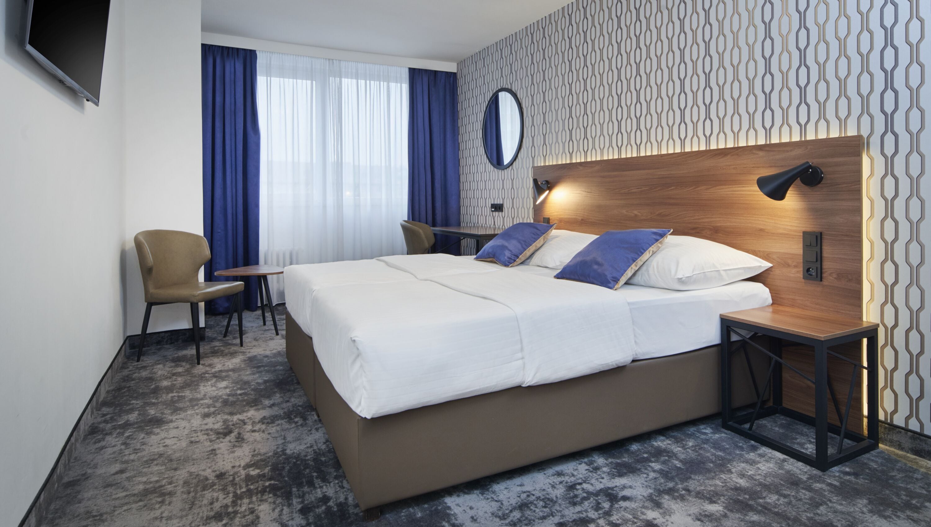 Una habitación de hotel moderna con una cama grande, un escritorio, una silla y un televisor instalado en la pared.