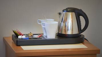 A coffee station with a kettle, two white mugs, and a tray with pens and a tissue.