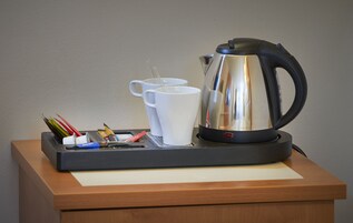 Kahvinurkkaus, jossa on vedenkeitin, kaksi valkoista mukea sekä alusta, jossa on kyniä ja paperinenäliinoja.