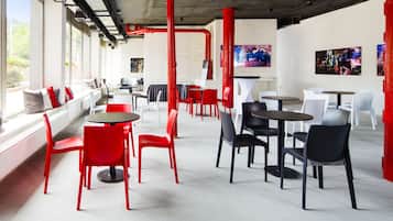 Cafetería interior con sillas y mesas rojas y blancas, y vistas al exterior con vegetación.