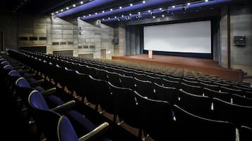 An indoor cinema with rows of seats, a large screen, and a stage.