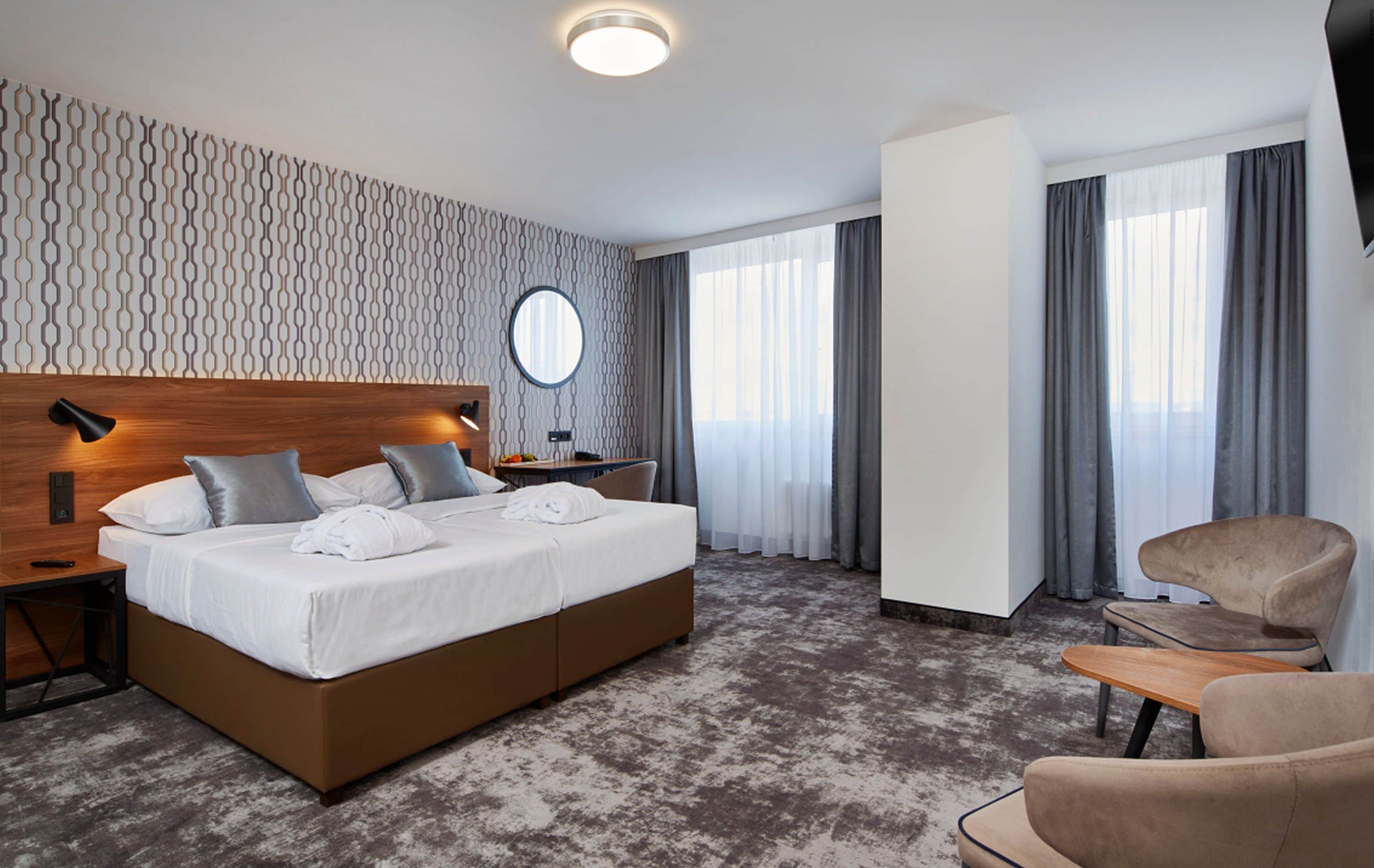 Una habitación de hotel moderna con una cama grande, una mesita de noche, un espejo redondo, un escritorio y una silla.