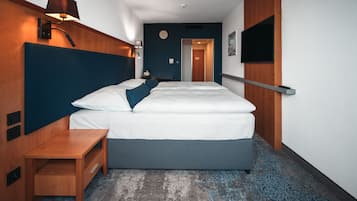 Habitación de hotel con una cama grande, mesita de noche, lámpara y televisor de pantalla plana montado en la pared.