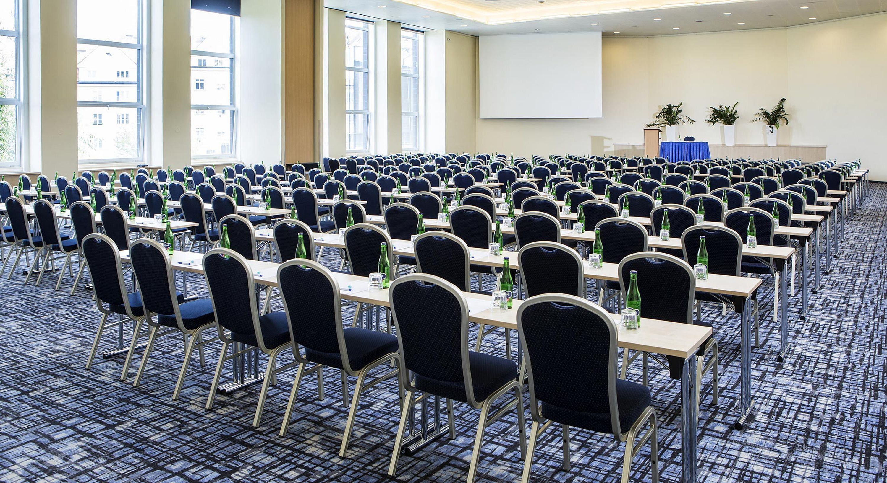 A conference room with rows of tables and chairs, large windows, and a presentation screen.