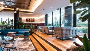 Un área de descanso moderna con distintos tipos de asientos, incluyendo sofás y sillones, piso de madera y ventanas grandes que ofrecen vistas al exterior.