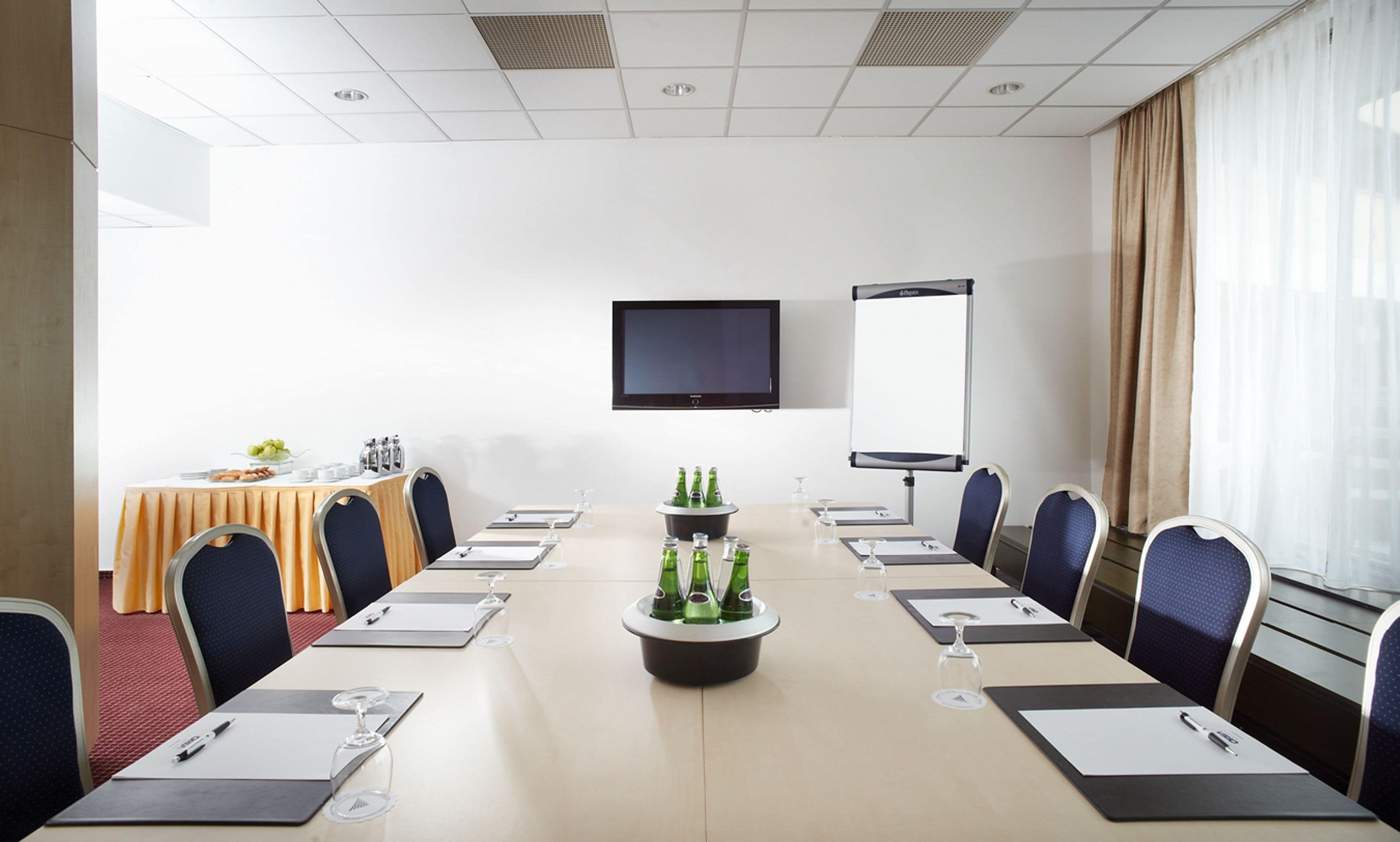 A conference room with a long table, chairs, a projector screen, and a screen on the wall.