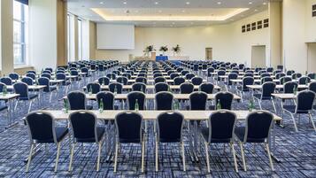 A large conference room with rows of tables and chairs, a projector screen, and large windows.