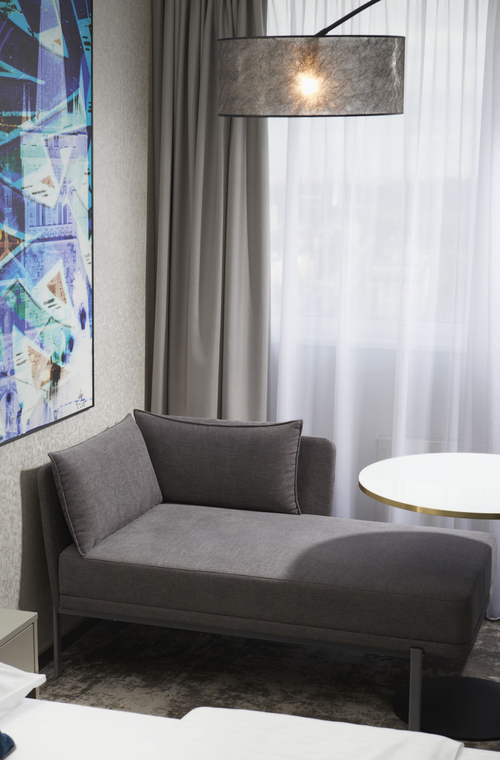 Una habitación moderna con un sofá gris, una mesa redonda y un cuadro abstracto grande en la pared.