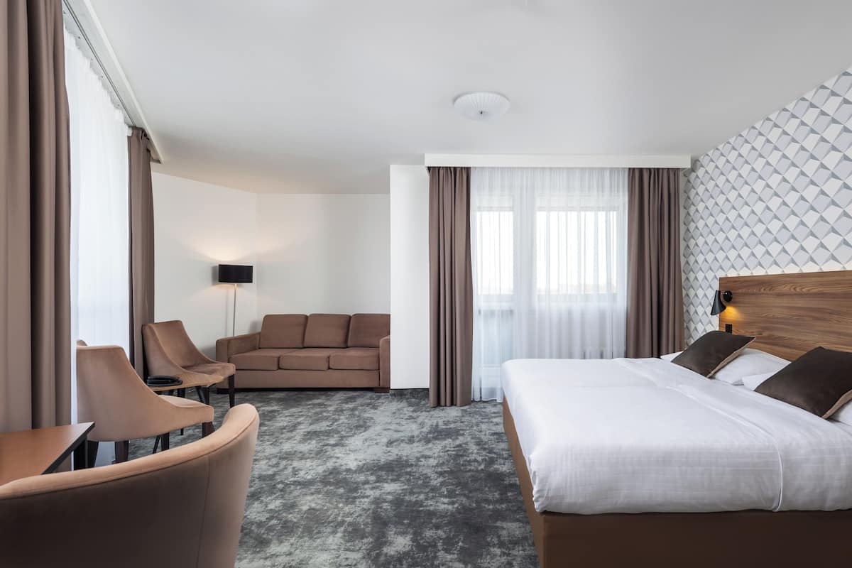 A hotel room with a bed, a sofa, a chair, a lamp, and a patterned wall.