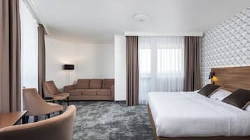 Quarto de hotel com cama, sofá, cadeira, abajur e parede estampada.