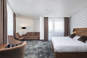 Quarto de hotel com cama, sofá, cadeira, abajur e parede estampada.
