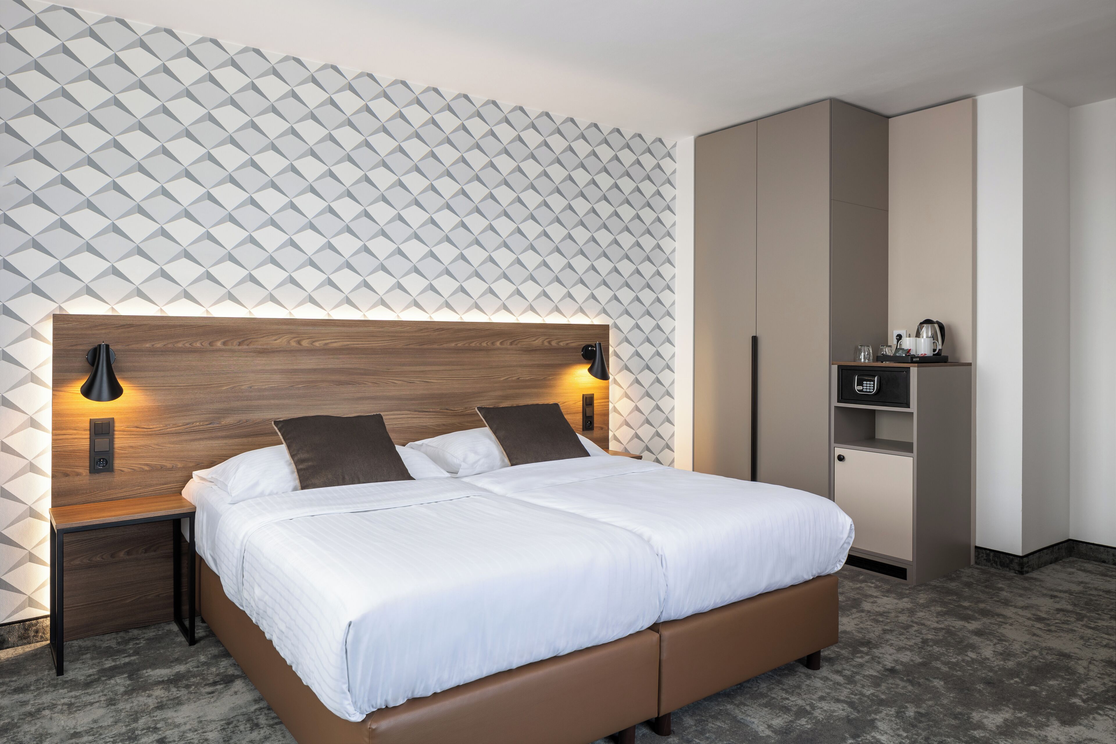 A modern bedroom with a wooden headboard, a bed with white linens, two bedside lamps, and a wardrobe.