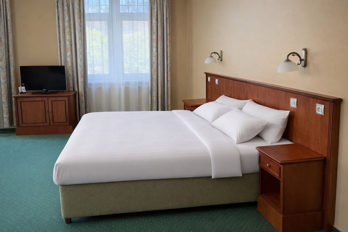 Quarto de hotel com uma cama grande, duas mesas de cabeceira, uma TV em um armário e uma janela com cortinas.