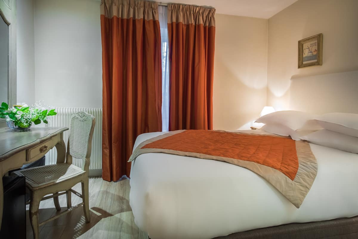 Camera d'albergo con un letto, una scrivania, una sedia e una finestra con tende.