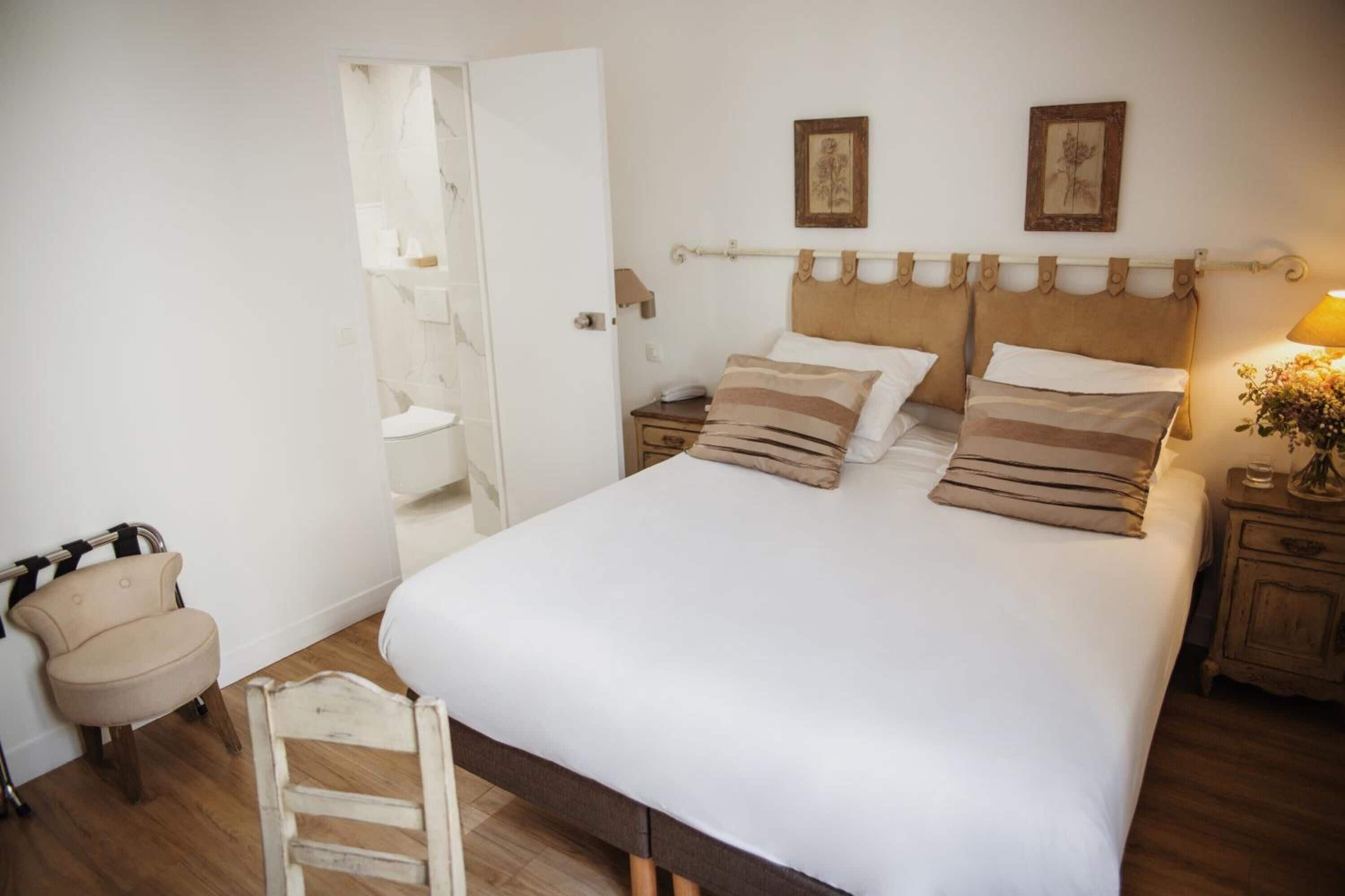 A bedroom with a large bed, a wooden nightstand, a chair, and a small table with a lamp.
