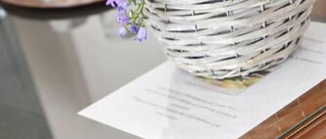 A wooden table with a glass top and a woven basket with purple flowers on it.