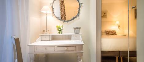A bedroom with a bed, a bedside table, a mirror, and a lamp.
