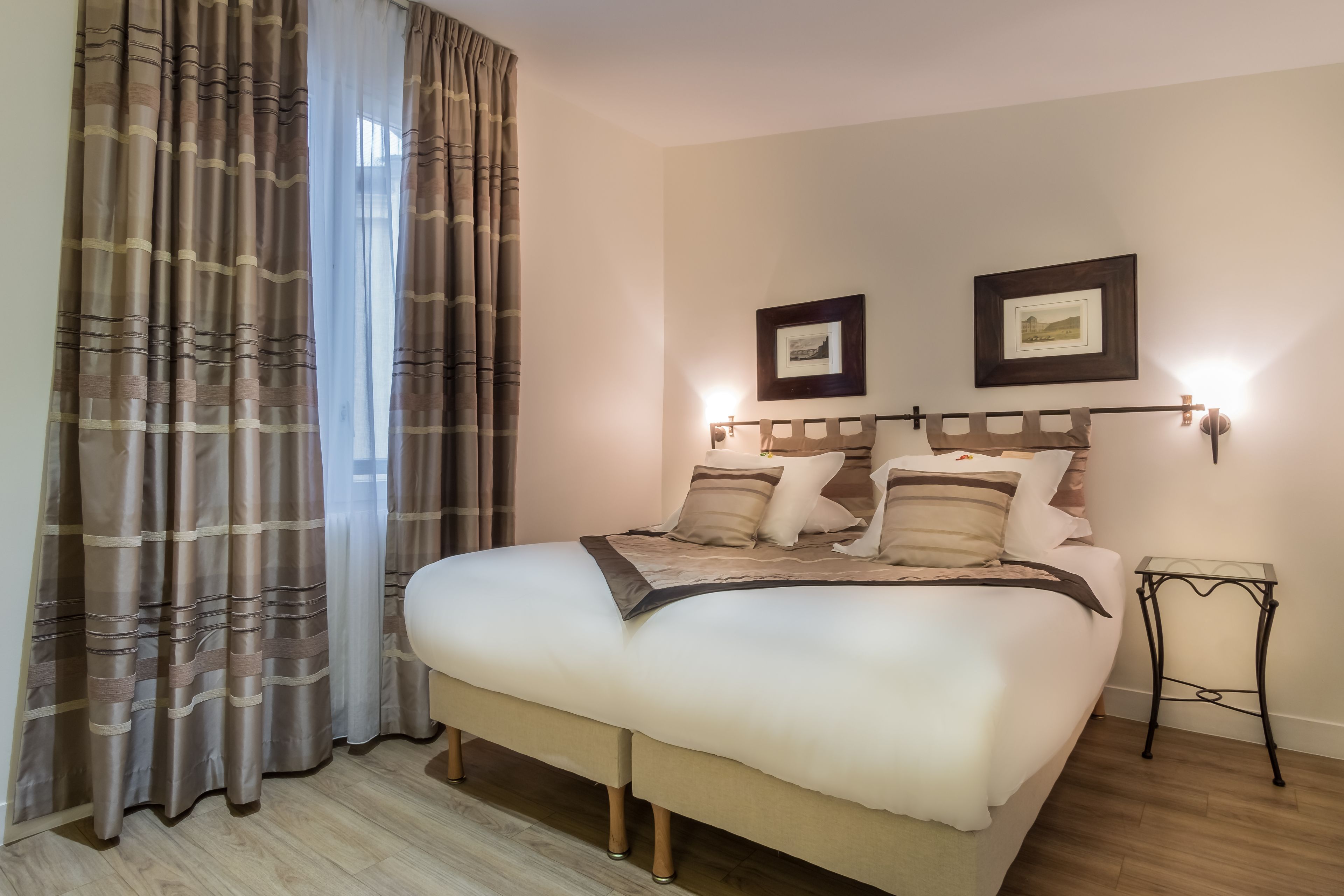 A neatly made bed with a headboard, a bedside table, and two framed pictures on the wall.