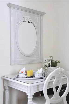 Uma mesa de jantar branca com uma bandeja de itens de café da manhã, uma cadeira branca e um espelho decorativo na parede.