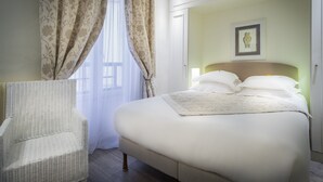 Un dormitorio ordenado con una cama, una silla y una ventana con cortinas.