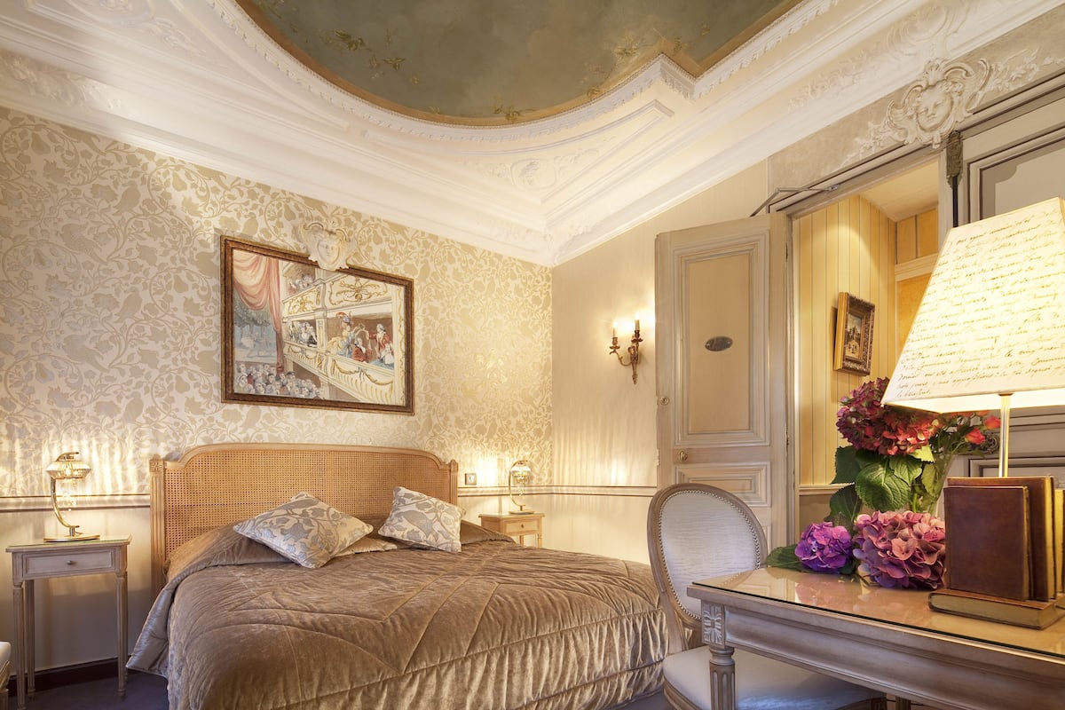 A well-appointed bedroom with a large bed, a desk with a lamp, and a mirror.