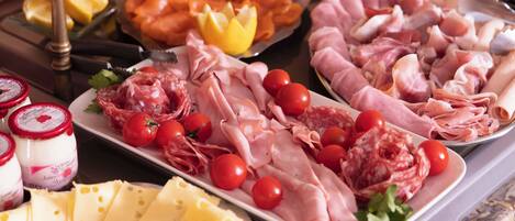 Une variété de fromages, de charcuteries et de tomates disposés sur une table de buffet.