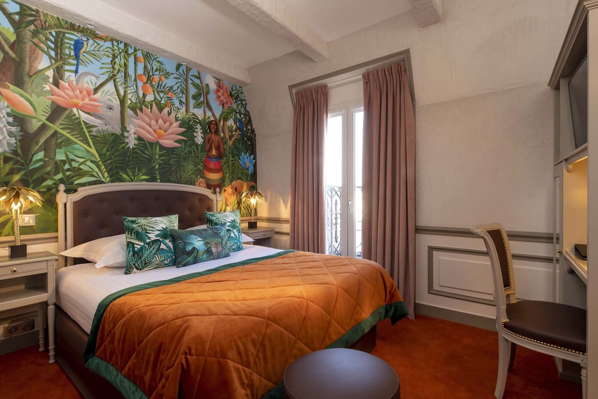 A bedroom with a large mural, a bed with a quilt, a nightstand, a chair, and a window with curtains.