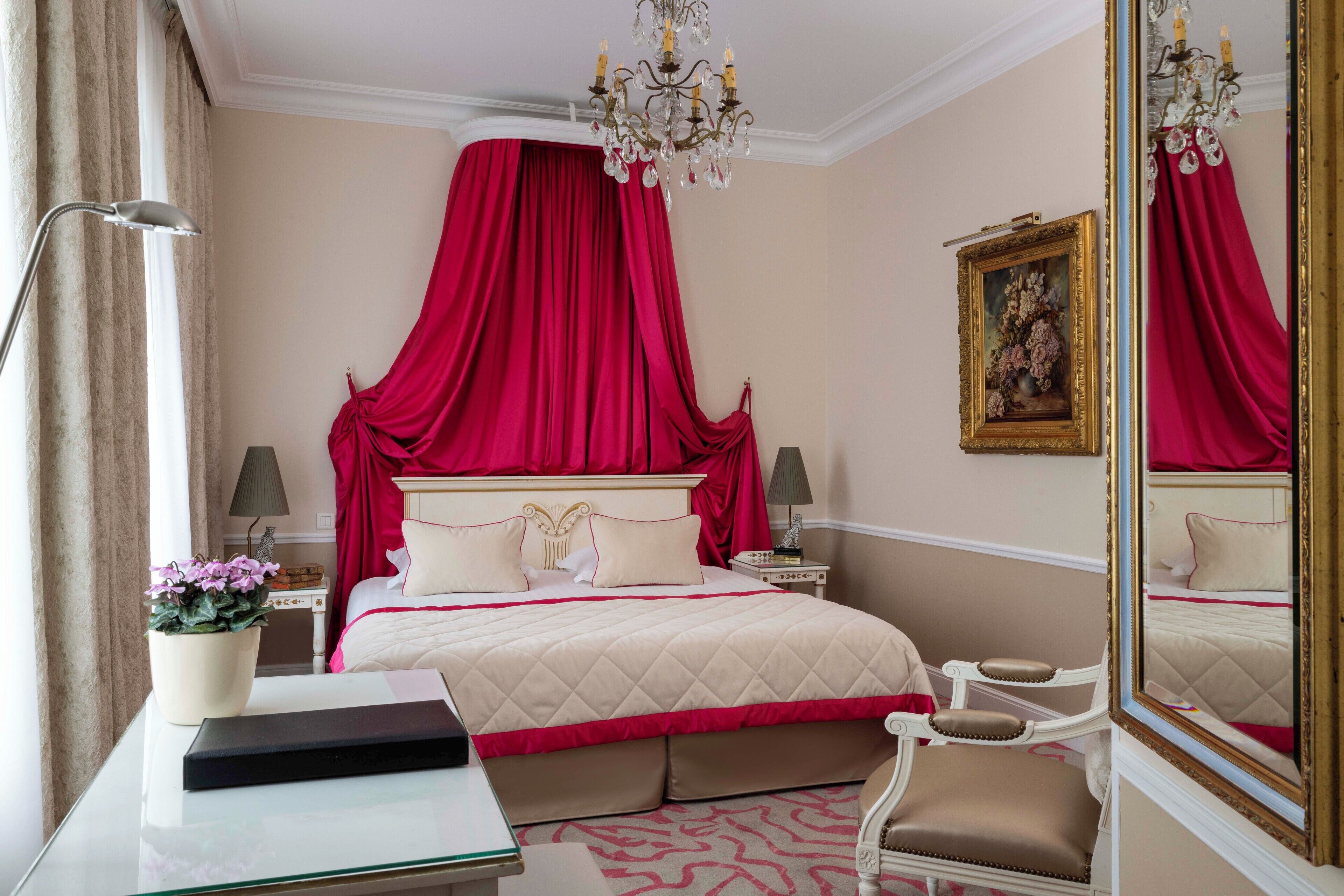 Una habitación de hotel con una cama grande, una araña, un espejo y un escritorio con lámpara.