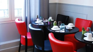 A corner dining area with a table set for two, red chairs, and a window with curtains. - Hôtel Cosy Monceau (Paris)