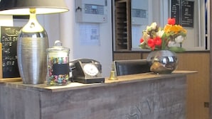 A reception desk with a lamp, a telephone, a vase with flowers, and a wall-mounted sign. - Hôtel Cosy Monceau (Paris)