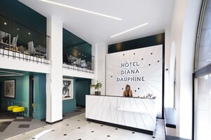 A modern hotel lobby with a reception desk, seating area, and a staircase.