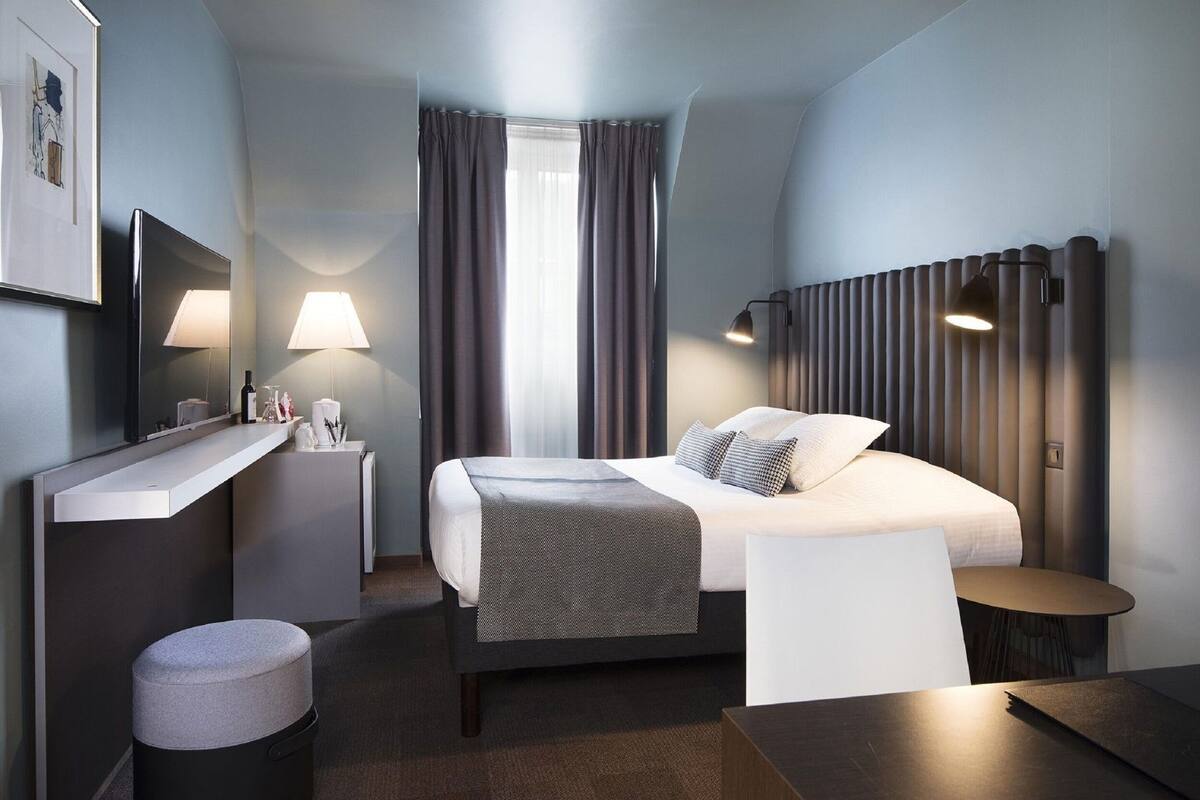 A modern hotel room with a bed, bedside tables, a desk, and a chair.