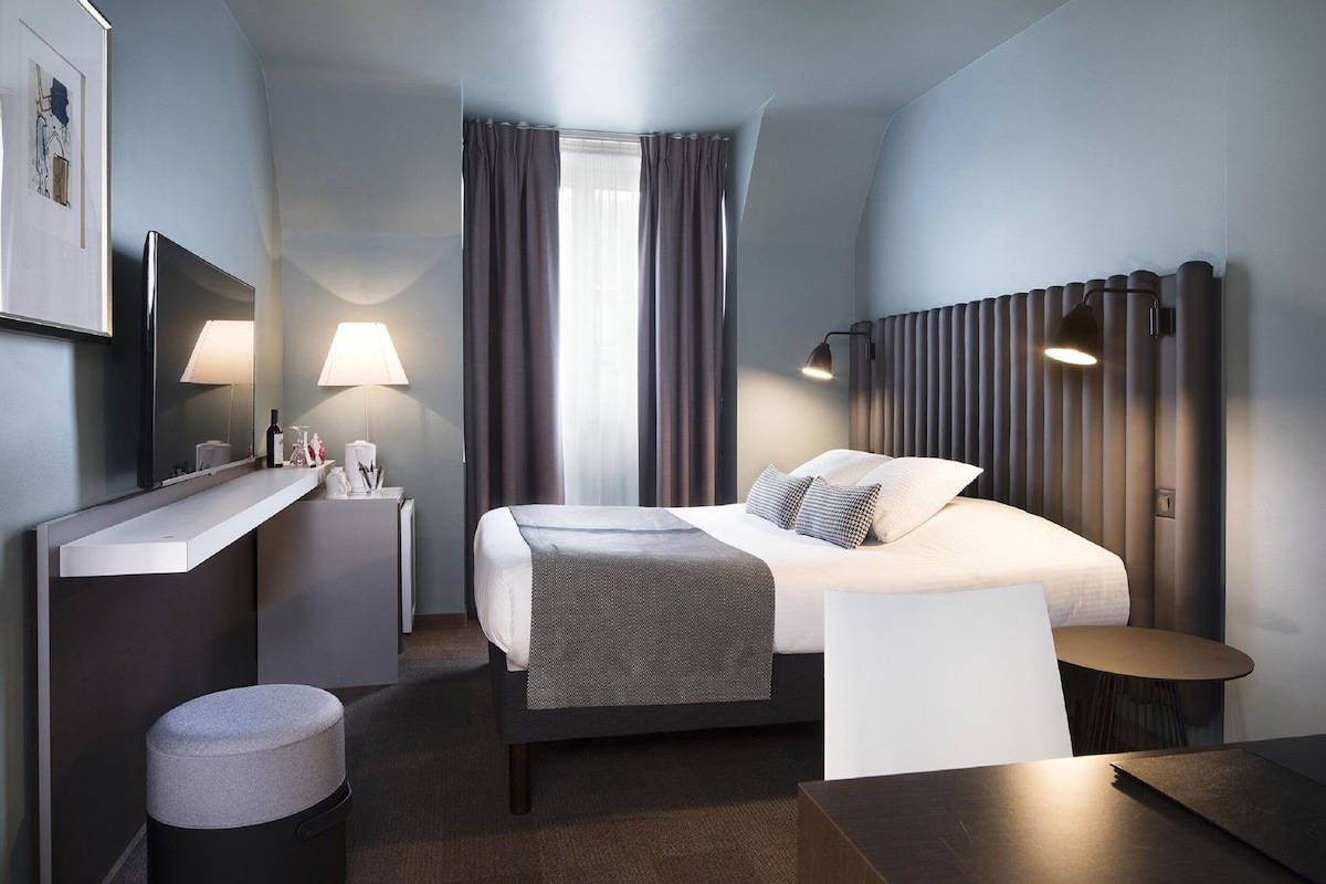 A modern hotel room with a bed, bedside tables, a desk, and a chair.